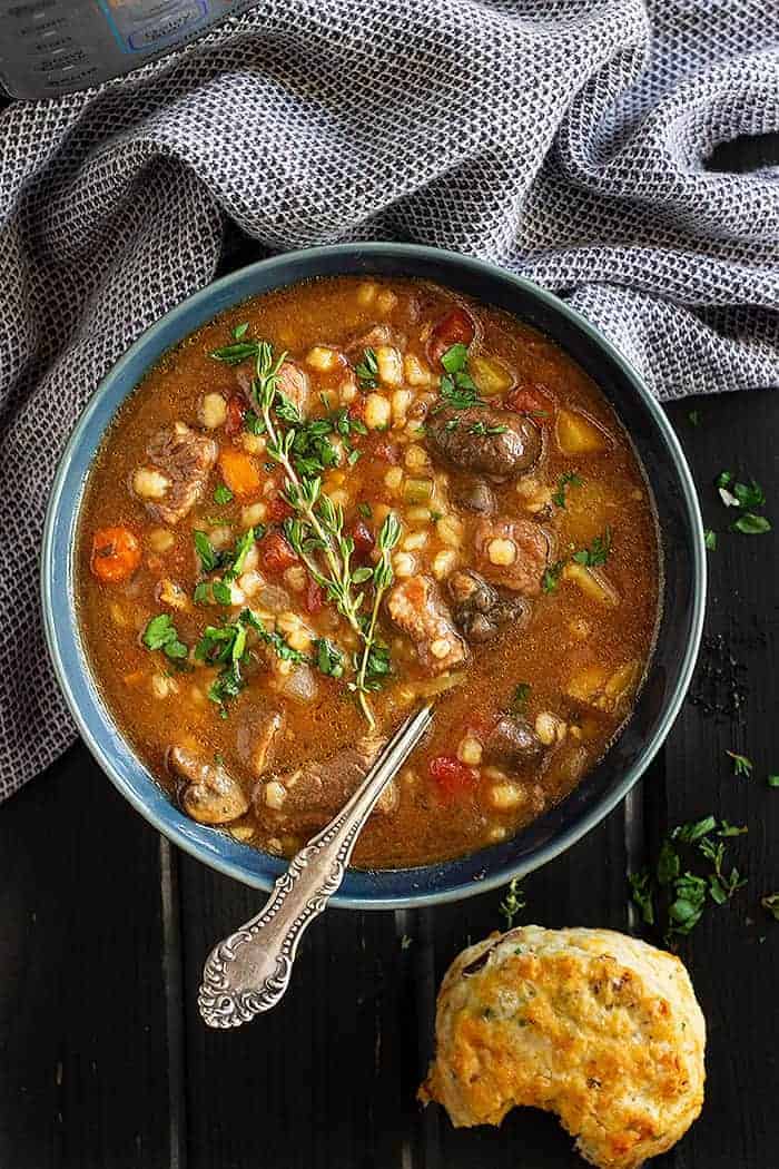 overhead: instapot beef barley soup in a blue bowl served with fresh biscuits