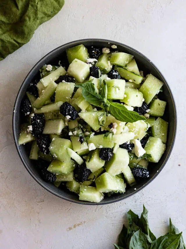 Overhead view of cucumber honeydew salad in a bowl with basil off to the side.