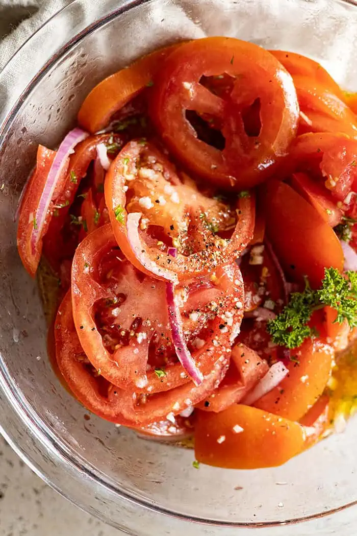 extreme closeup: my marinated tomato recipe in a bowl garnished with cracked pepper and flaky salt