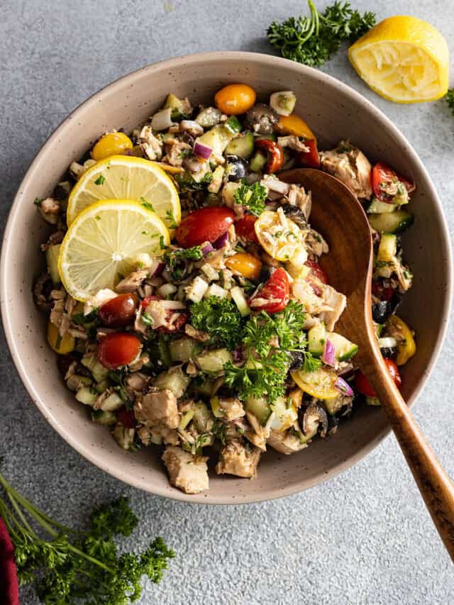 Overhead view of tuna salad in a large bowl with wooden spoon in it. Garnished with fresh herbs and lemon slices.