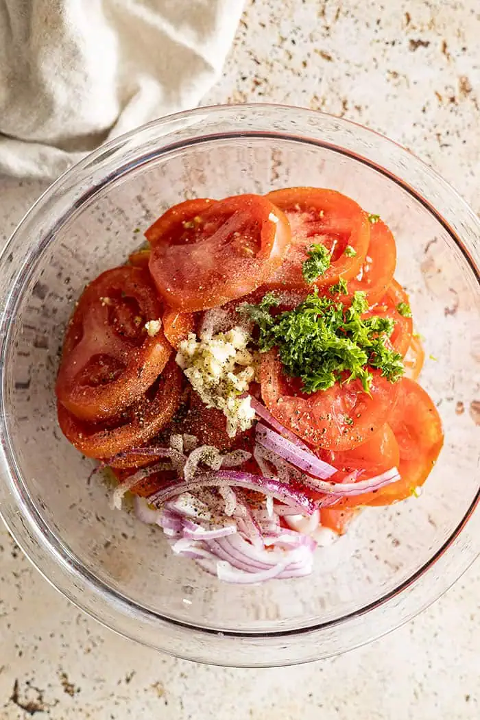 overhead closeup: all the ingredients for this recipe for marinated tomatoes in a bowl ready to be mixed