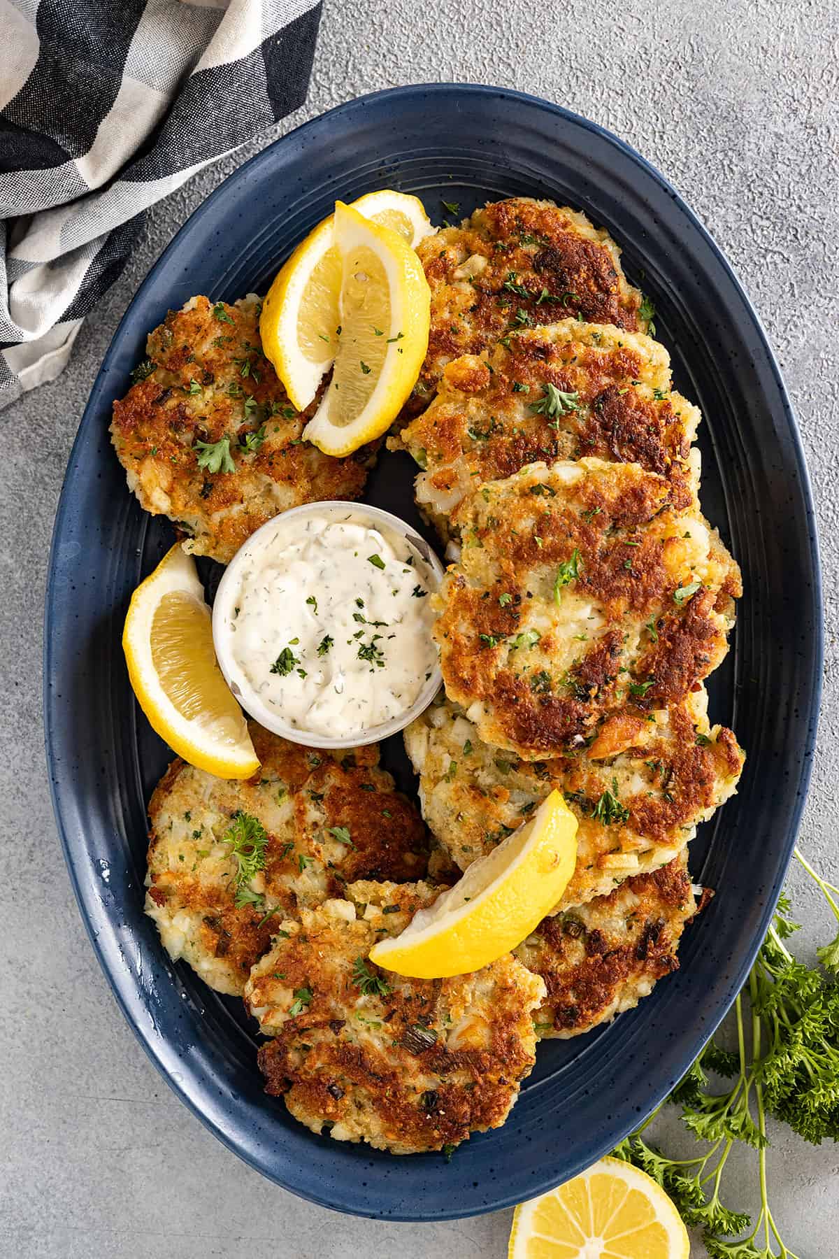 Overhead view of fish cakes on a dark blue plate and garnished with lemon wedges and tarter sauce.
