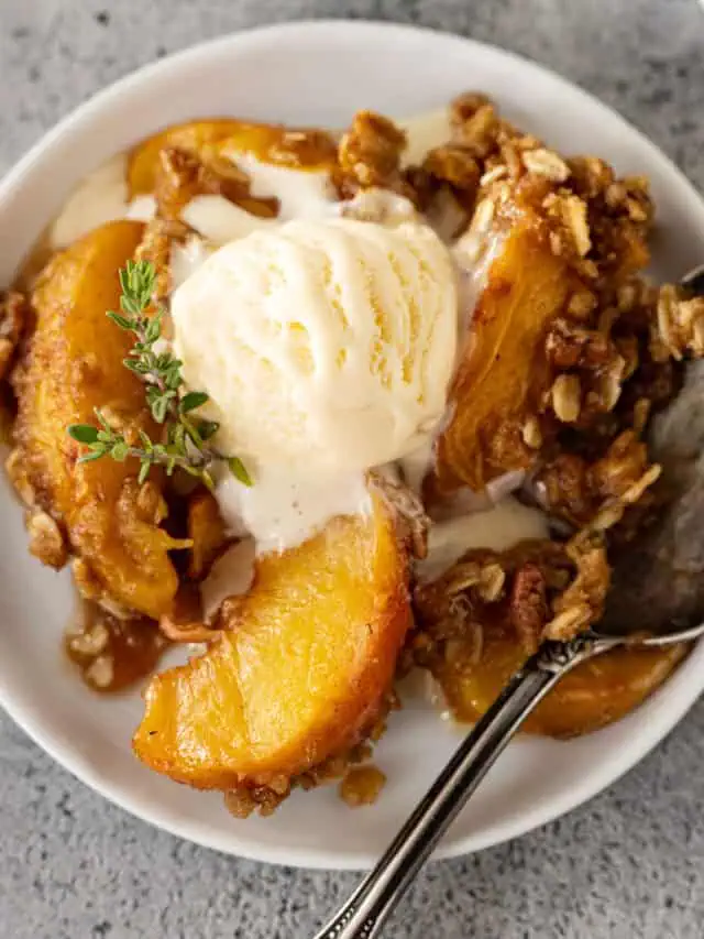 Overhead view of peach crisp on a white plate with ice cream slowly melting into the crisp.
