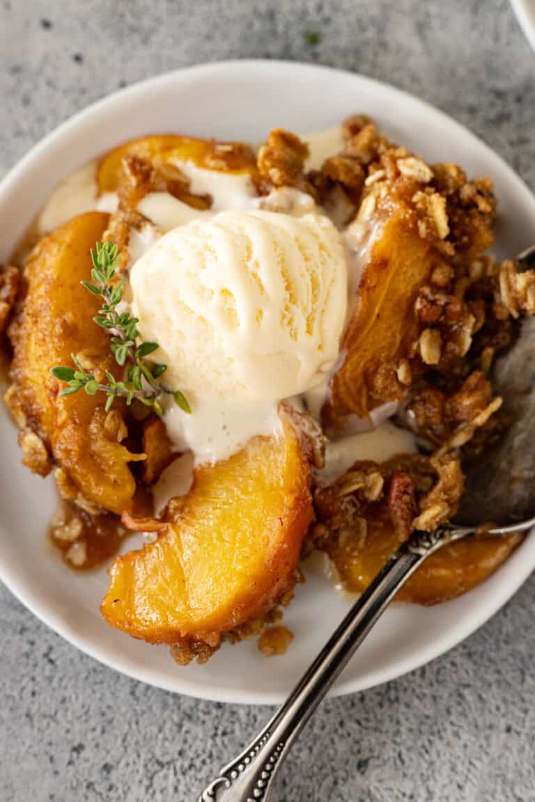 Overhead view of peach crisp on a white plate with ice cream slowly melting into the crisp.