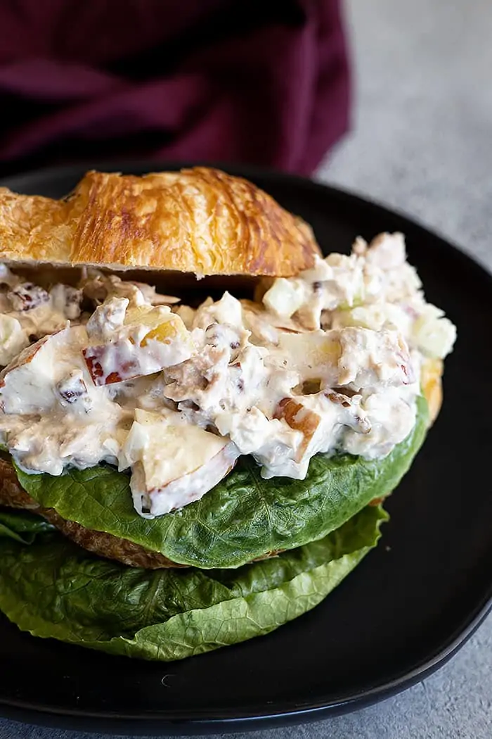 closeup: tuna salad with apples piled on a buttery croissant with a leaf of lettuce