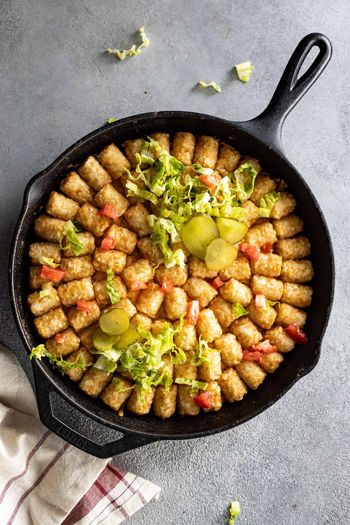 Overhead view of big mac casserole in a cast iron skillet garnished with pickles, tomatoes, and lettuce. 