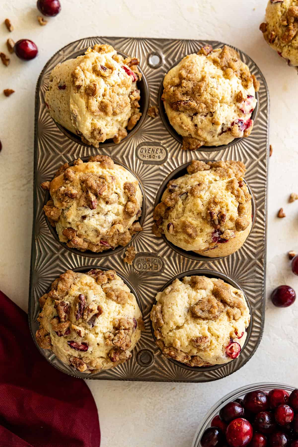 Overhead view of muffins in a muffin tin. Fresh cranberries scattered off to the sides and a red napkin in the corner. 