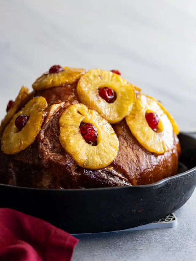 Pineapple ham in a cast iron skillet with red napkin off to the side.
