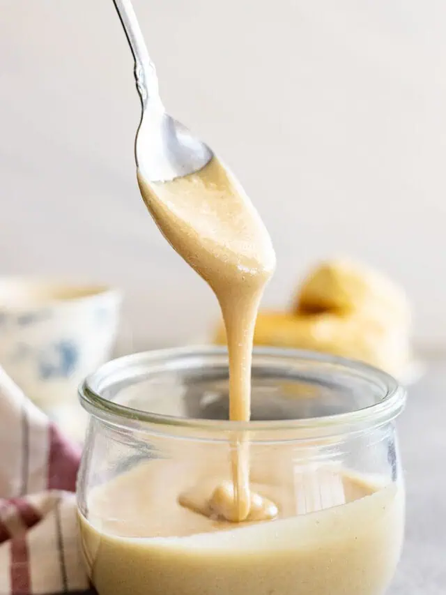 Spoon pulling up whipped honey from a jar.