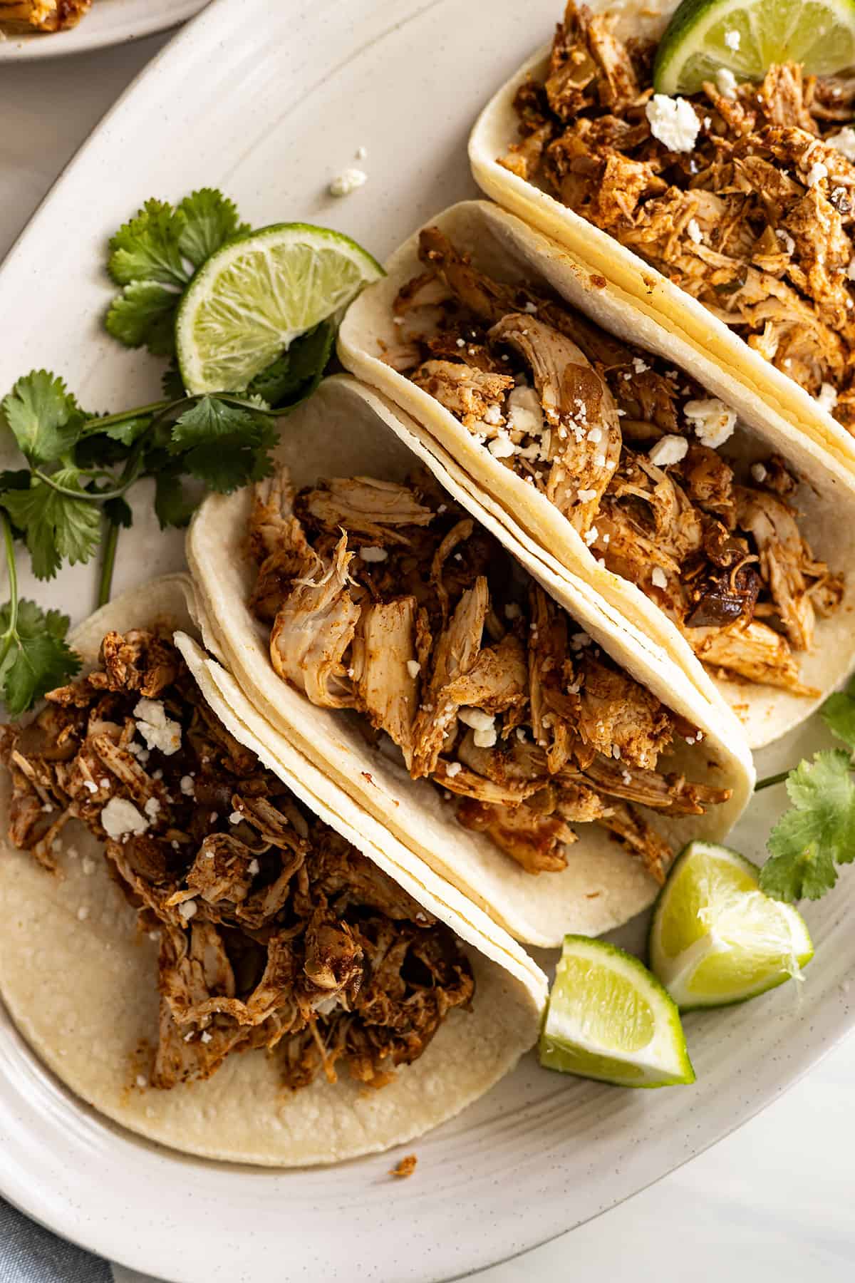 Overhead view of tacos on a white plate garnished with white cheese. 