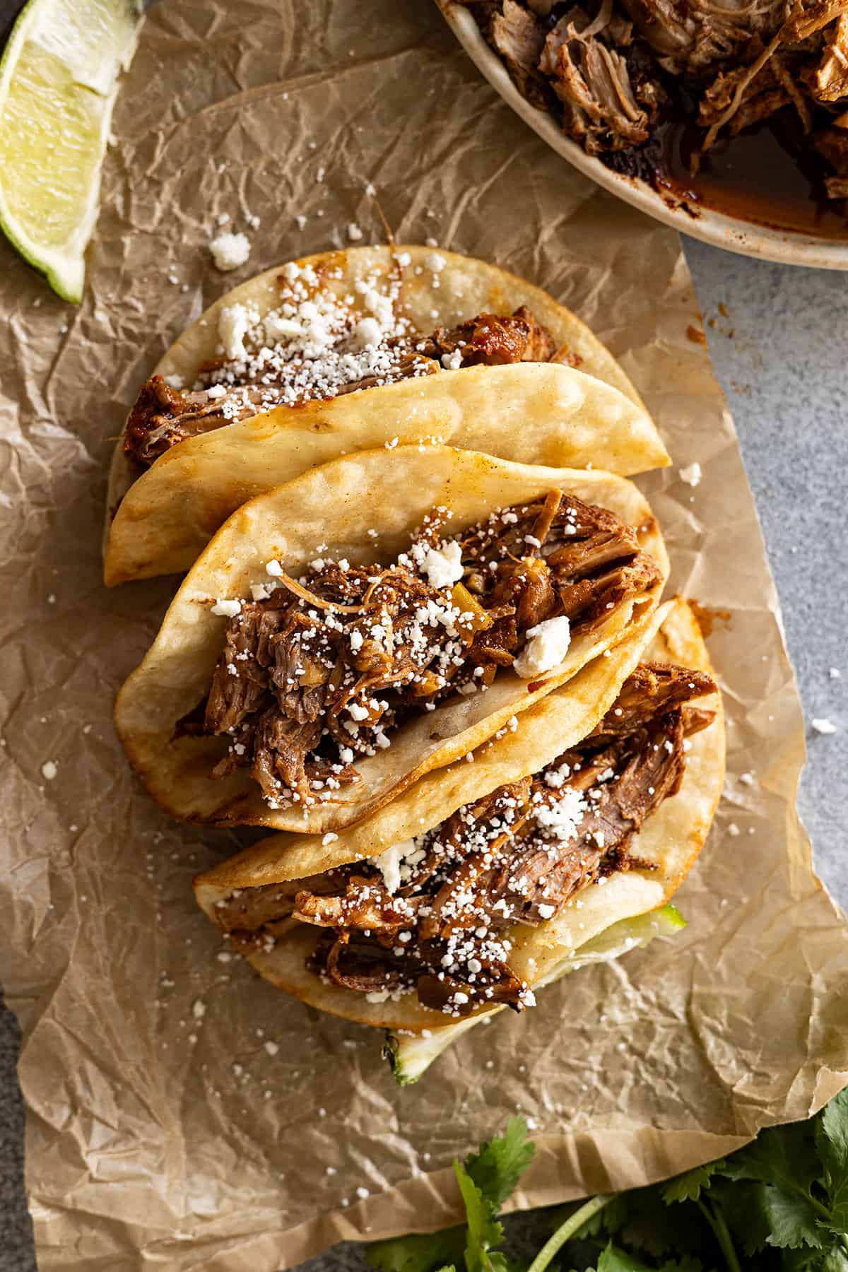 Overhead view of pork tacos on a piece of brown parchment sprinkled with cheese.