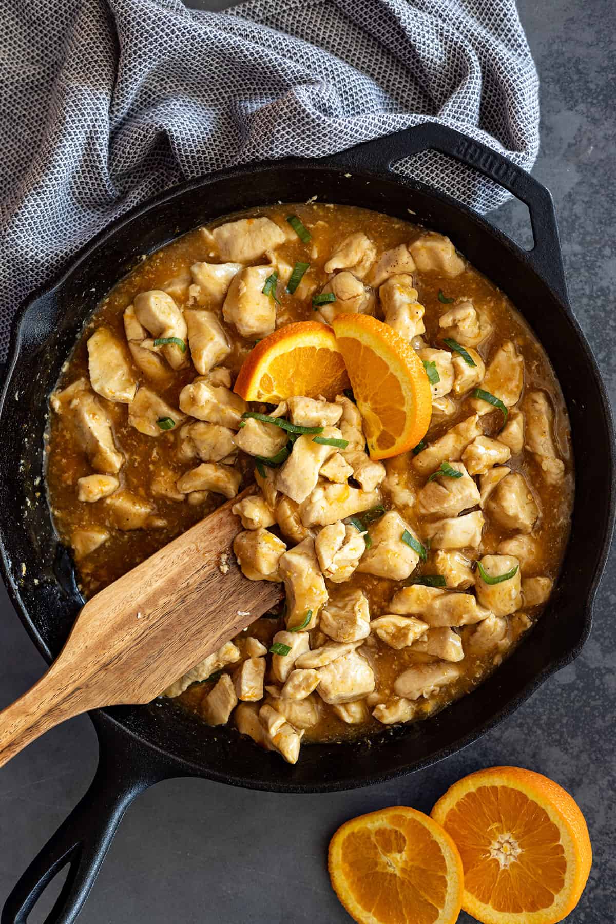 Orange chicken in a cast iron skillet garnished with orange slices. 