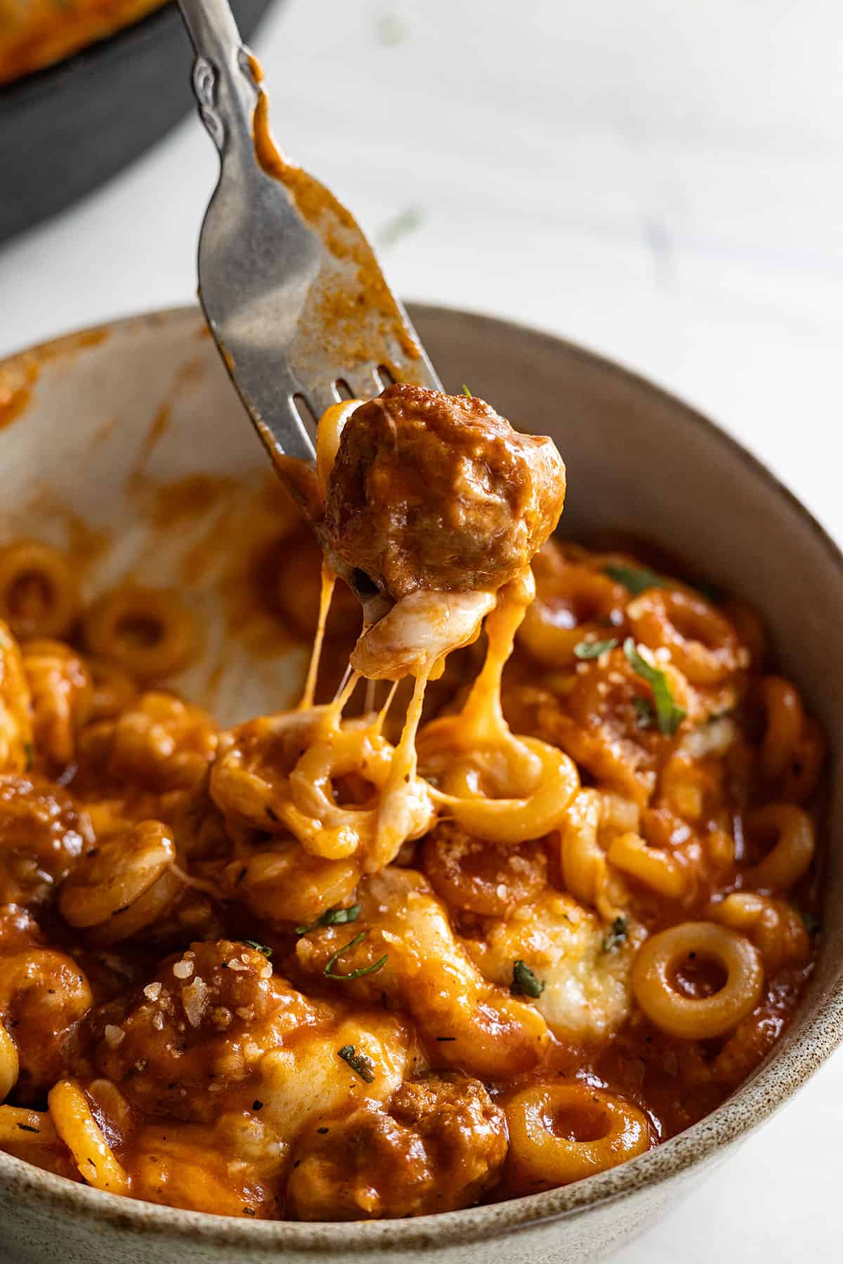 A meatball on a fork being pulled up from the bowl of spaghettios. 