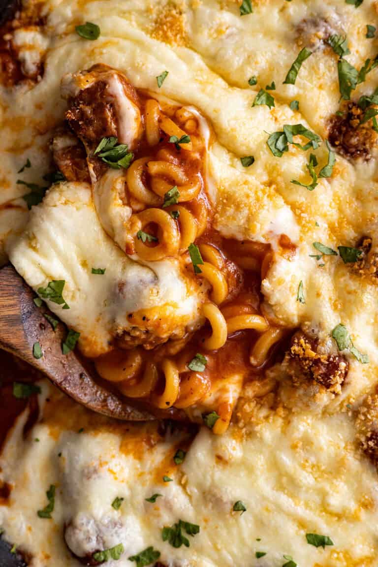 Close up of cheesy spaghettios with meatballs with a spoon in it.
