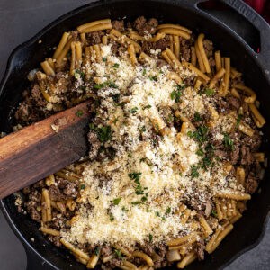Overhead view of pasta in a cast iron skillet with parmesan and chopped parsley sprinkled on top.