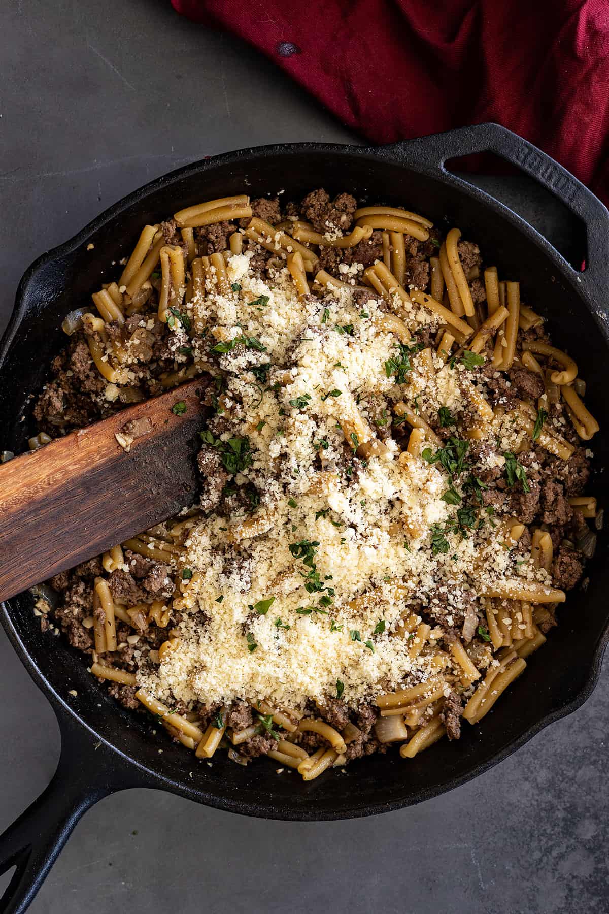 Overhead view of pasta in a cast iron skillet with parmesan and chopped parsley sprinkled on top. 