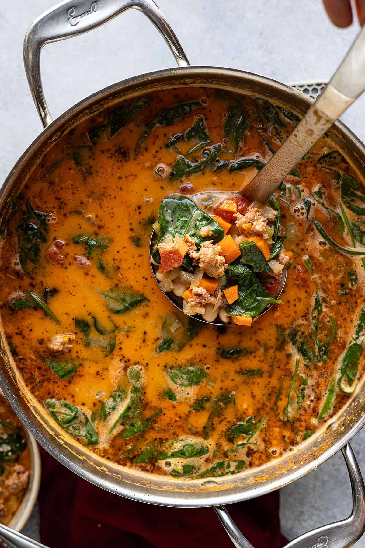 Ladle pulling up tuscan white bean soup ready to serve to bowls. 