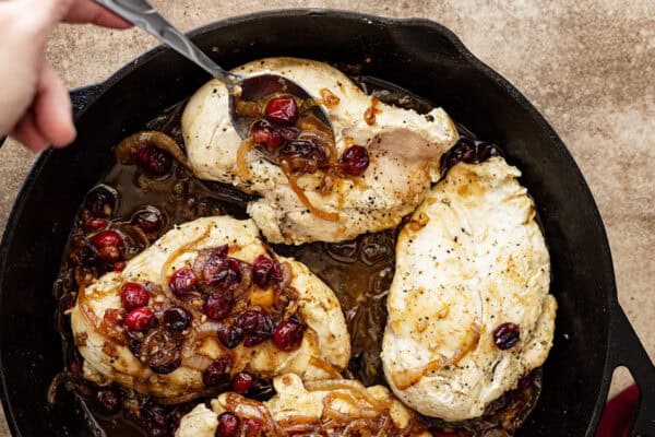 A spoon ladling the onion cranberry sauce on top of the chicken breasts.