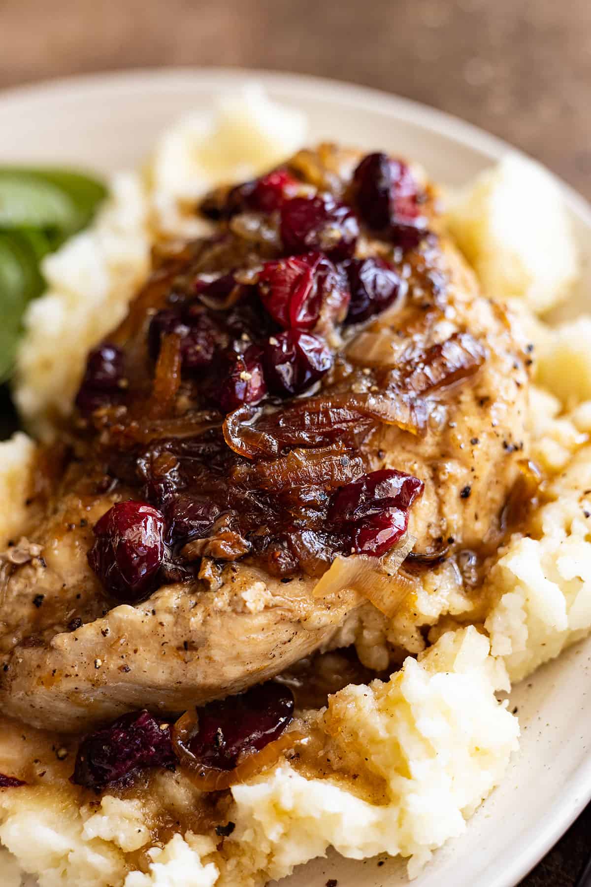 Chicken breast piled high with caramelized onions and cranberries on top of a bed of fluffy mashed potatoes. 