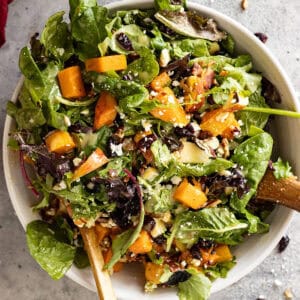 Overhead view of salad in a white bowl with salad tongs.