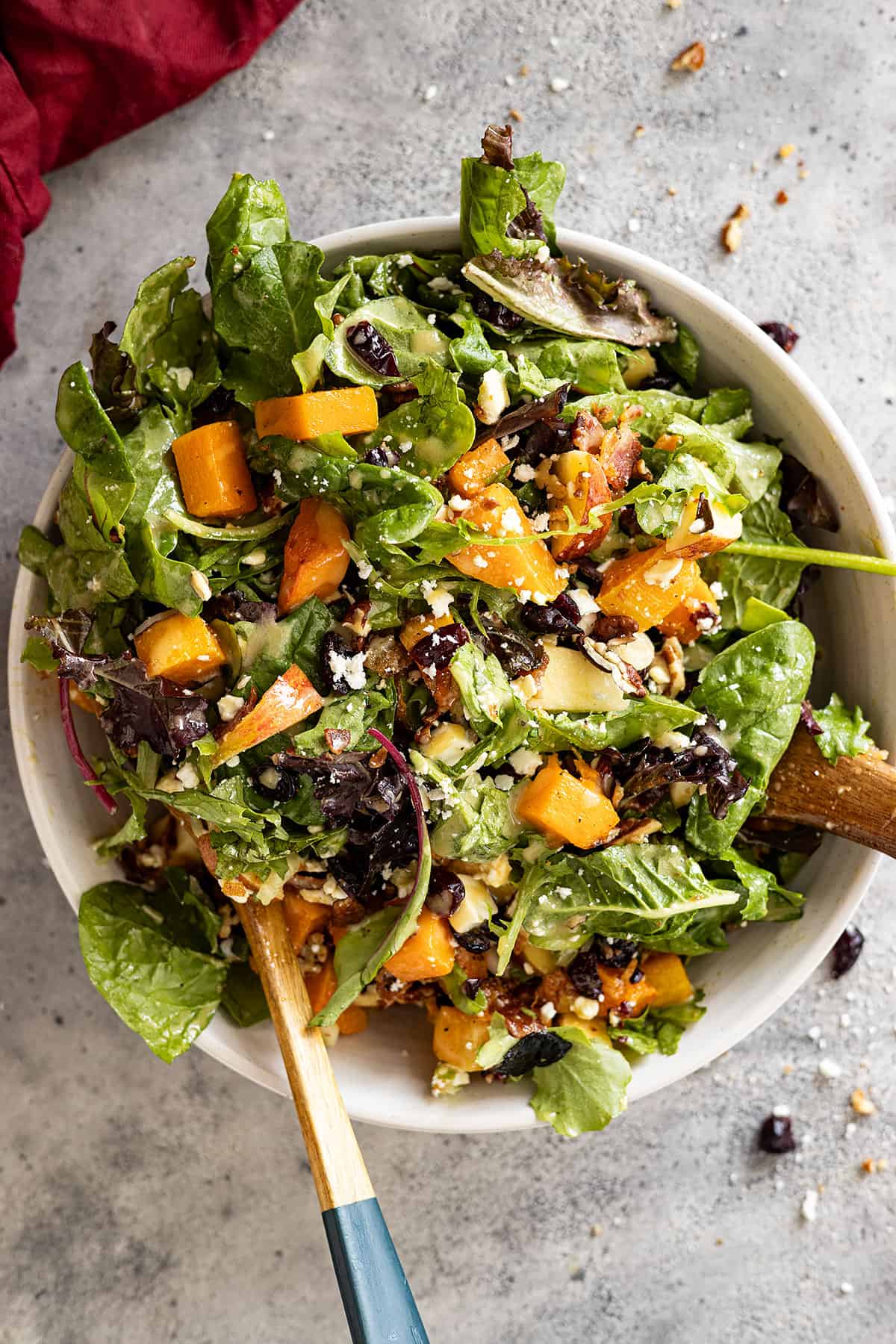 Overhead view of butternut squash salad in a white bowl with salad tongs.