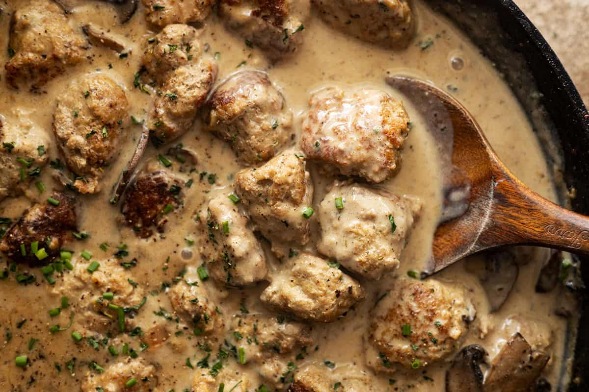 close up of meatballs in gravy with a spoon. 