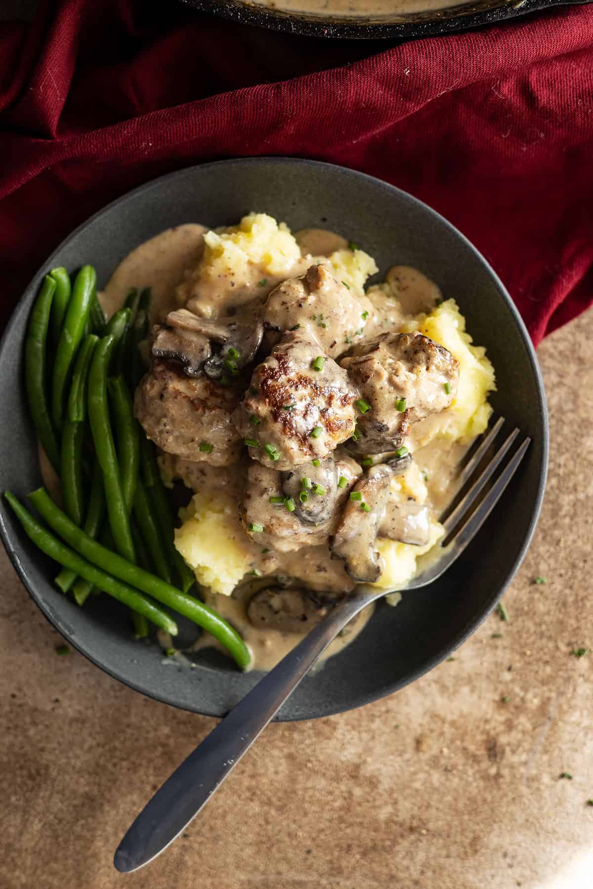 turkey meatballs in creamy mushroom gravy on a plate on top of mashed potatoes with green beans on the side. 
