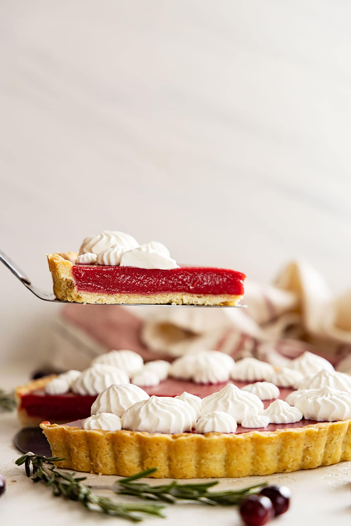 a slice of cranberry curd tart being held above the tart. can see the lovely layers of the whipped topping, cranberry curd, and crust. 