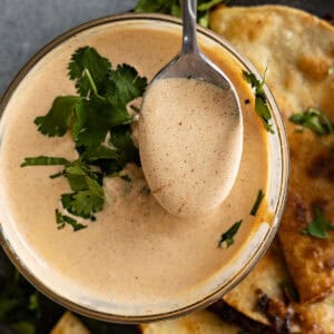 A spoon pulling up sauce from the bowl ready to drizzle over tacos.