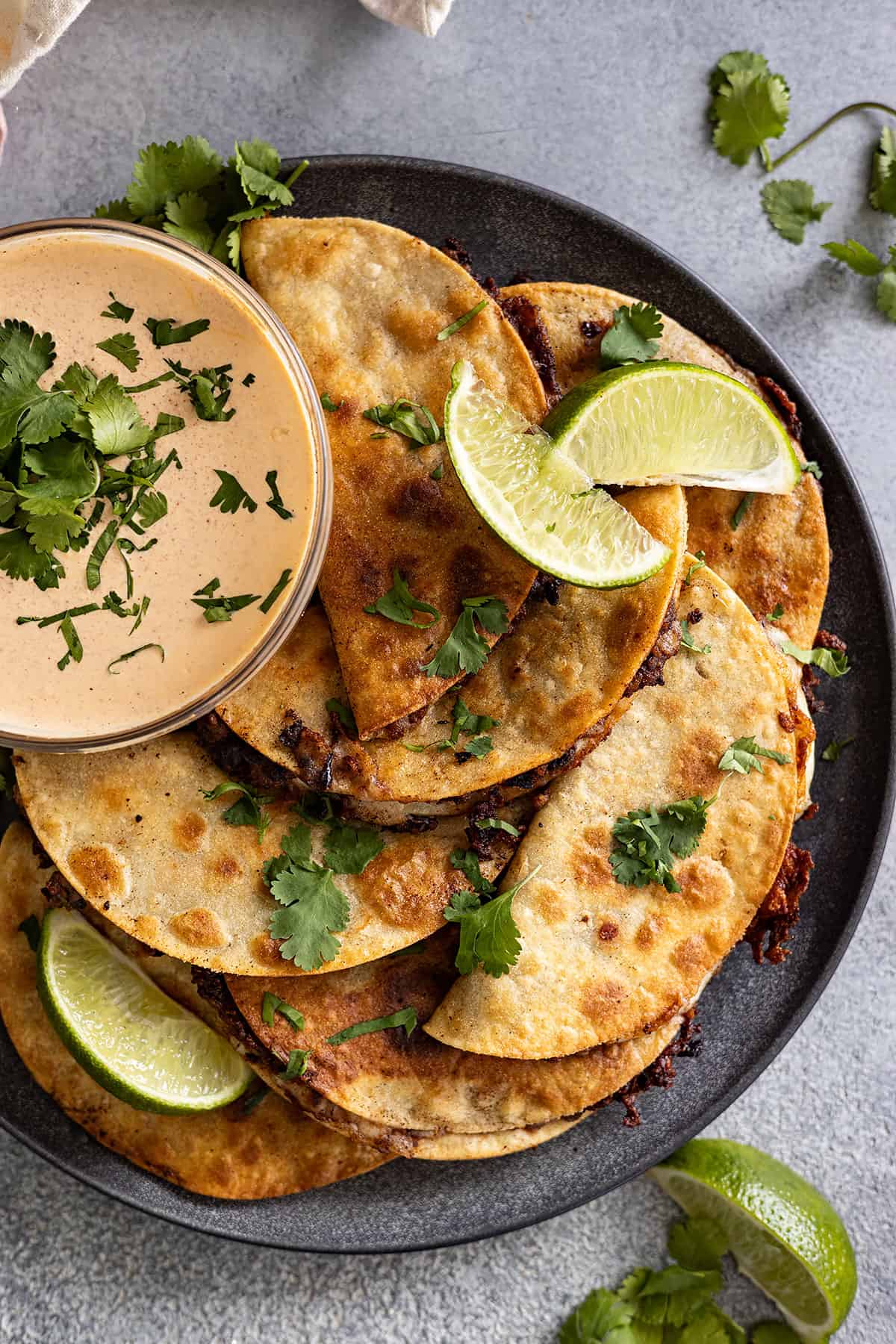 Overhead view of crispy black bean tacos stacked on a plate with a bowl of sauce on the side.