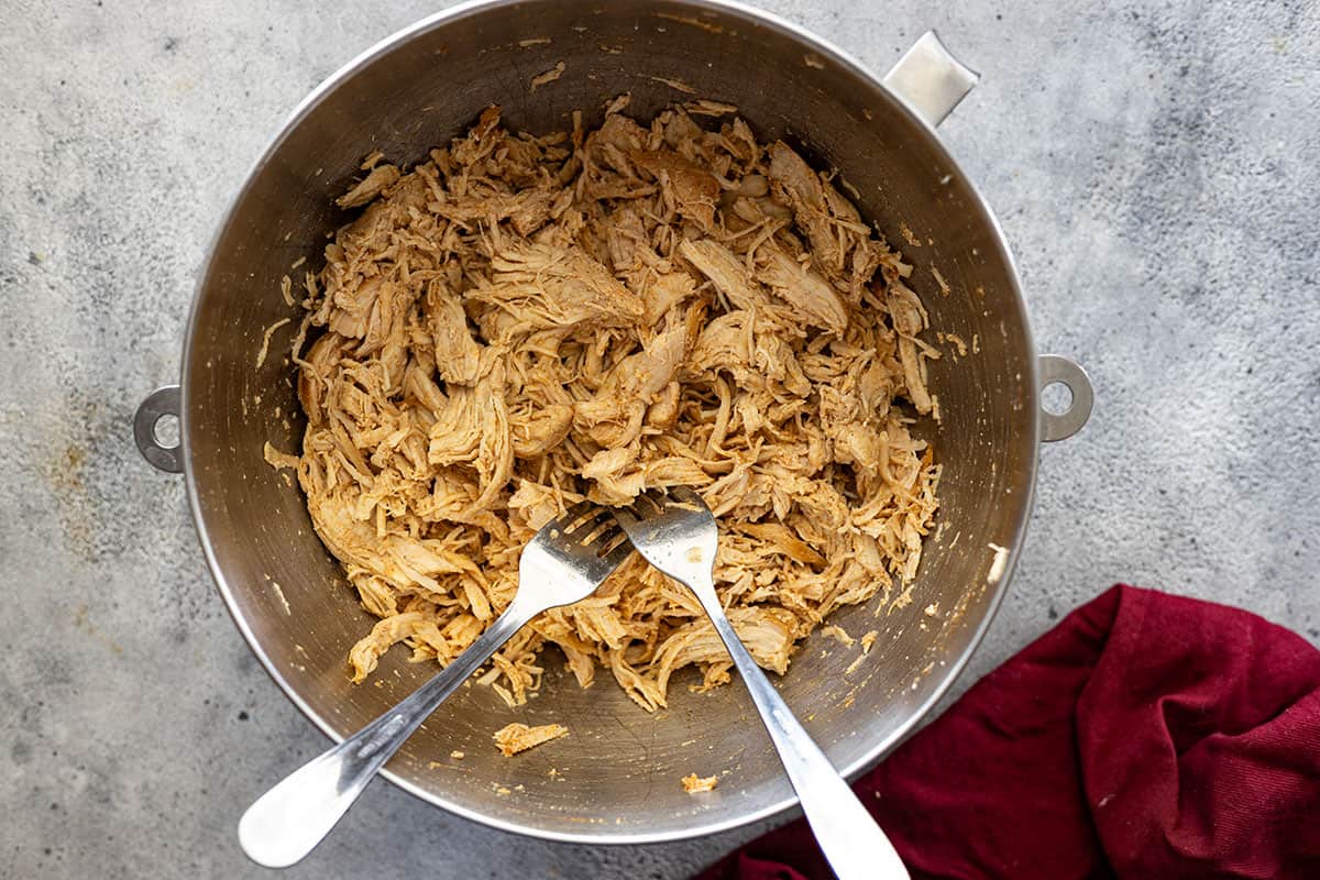 Overhead picture of chicken shredded up in a bowl with two forks.