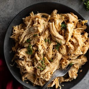 Overhead picture of juicy shredded chicken on a dark plate garnished with parsley.