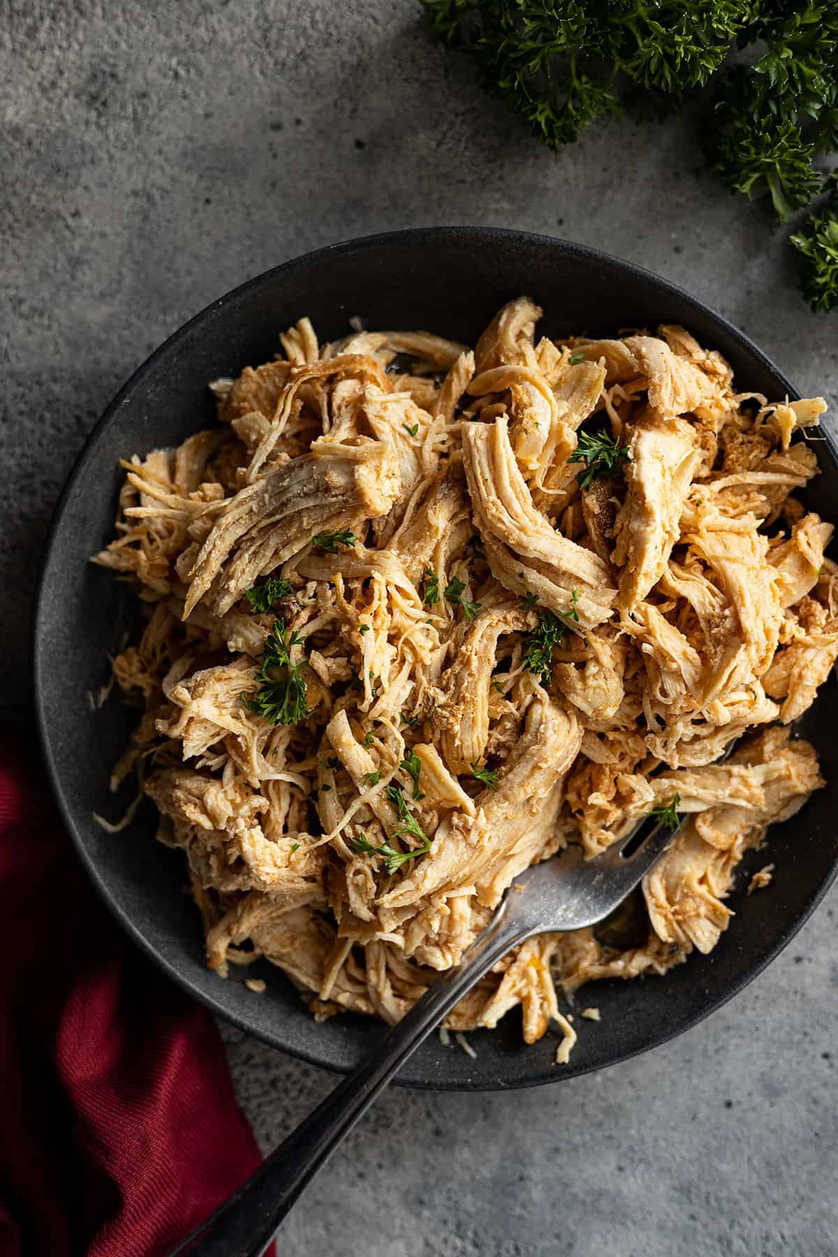 Overhead picture of juicy shredded chicken on a dark plate garnished with parsley.