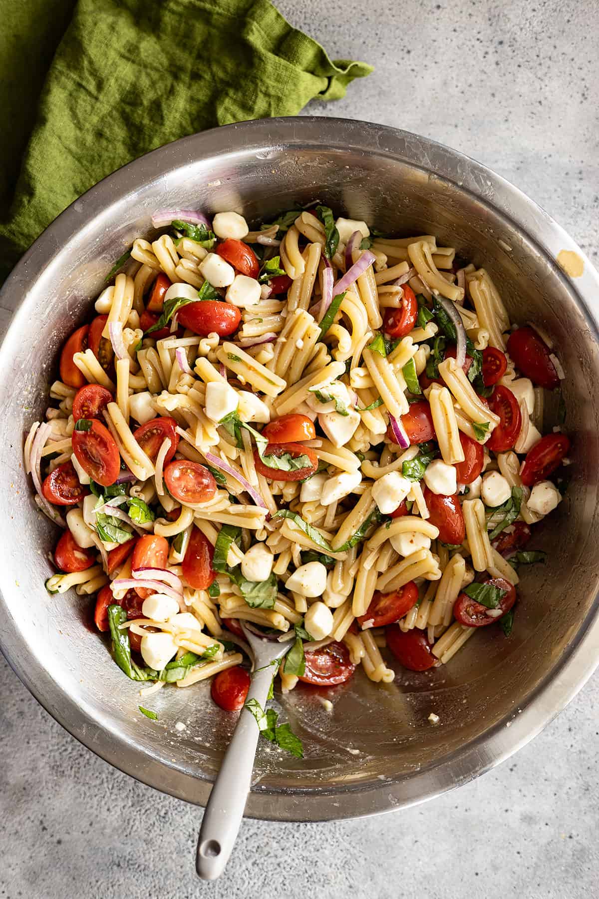 Overhead view of bruschetta pasta salad in a large with a green napkin off to the side.