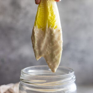 Lettuce being pulled up out of a jar of homemade caesar dressing.