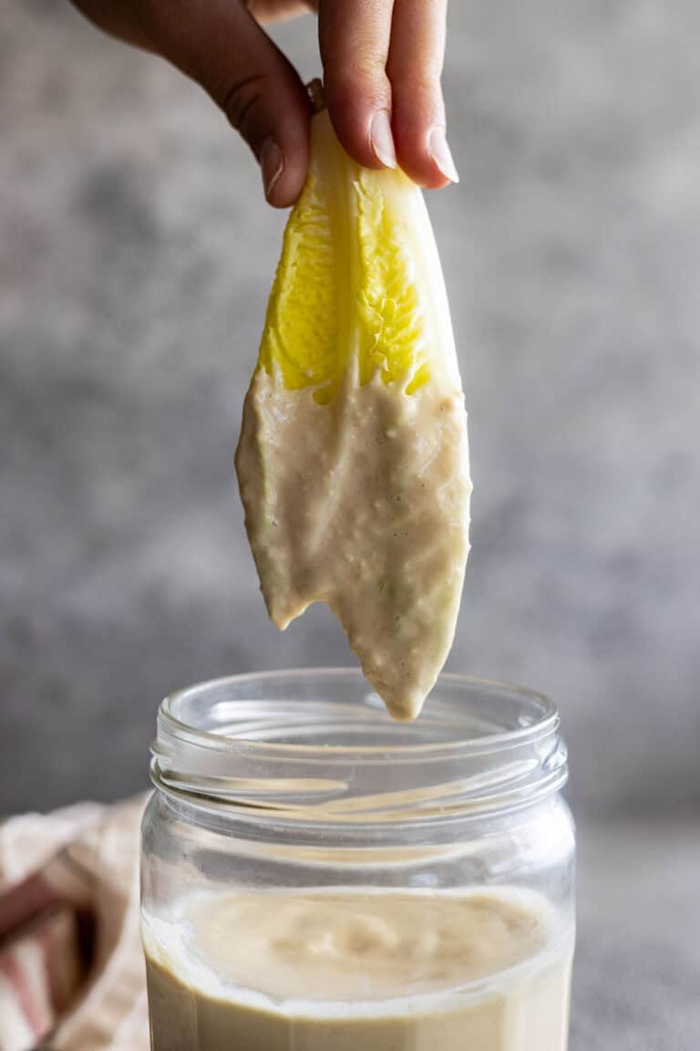 Lettuce being pulled up out of a jar of homemade caesar dressing.