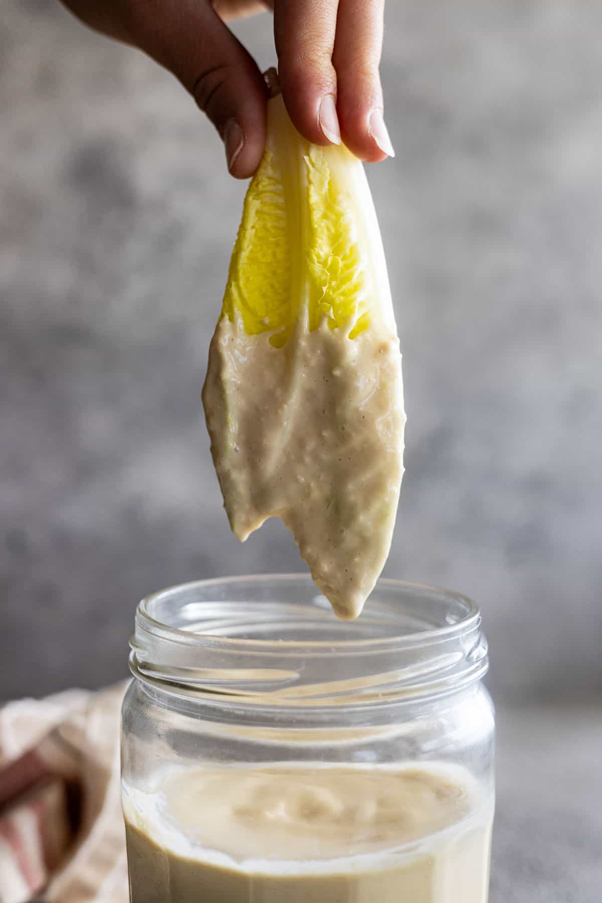 Lettuce being pulled up out of a jar of homemade caesar dressing.