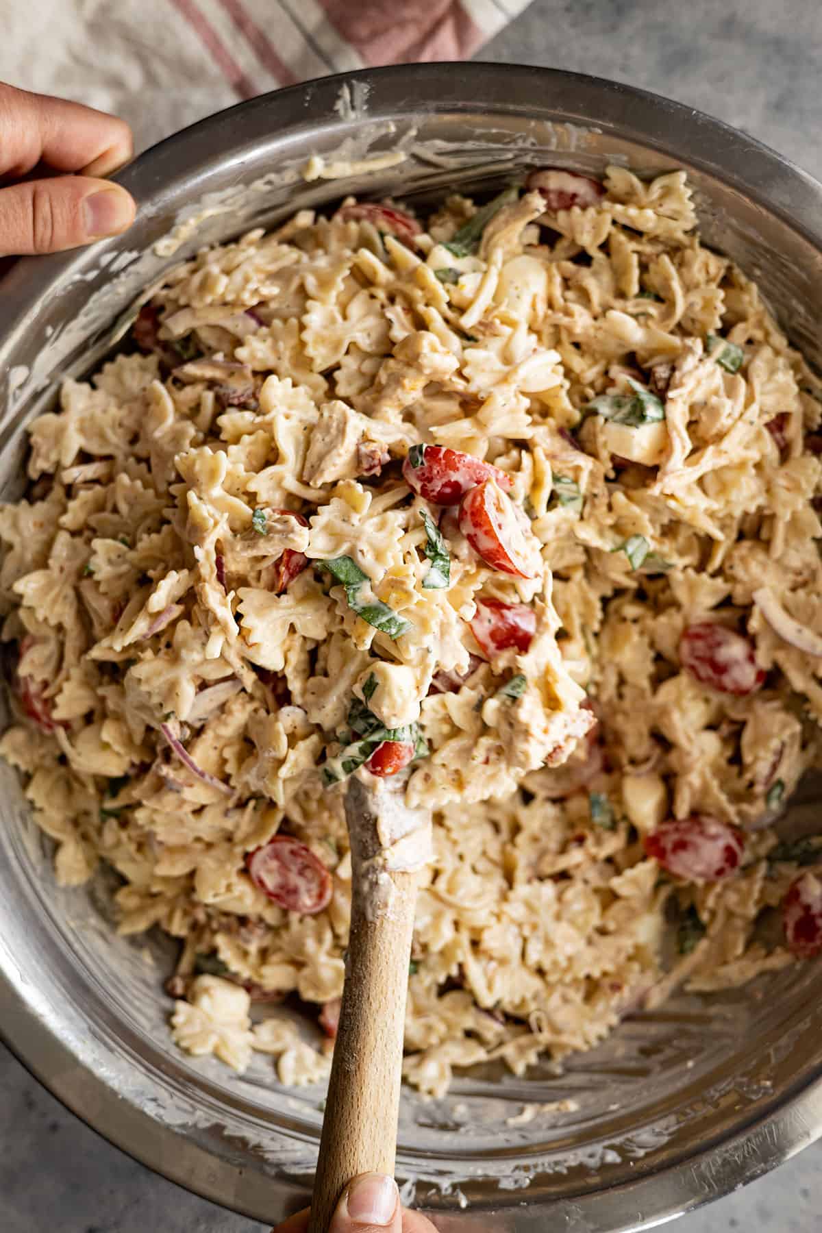 Overhead view of pasta salad being mixed with a wooden spoon.