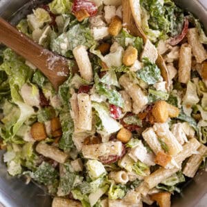 Overhead view of chicken caesar pasta salad in a bowl with spoons ready to serve it.