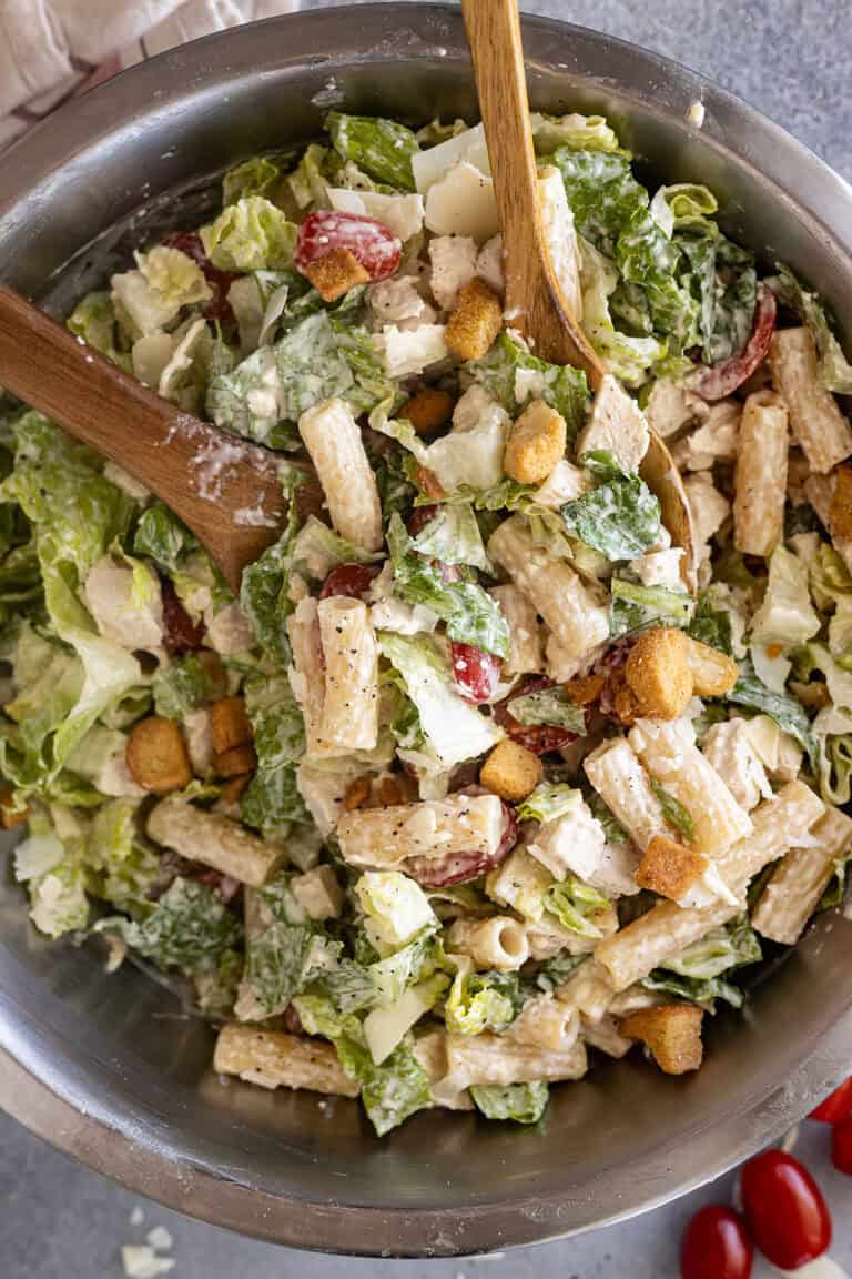 Overhead view of chicken caesar pasta salad in a bowl with spoons ready to serve it.