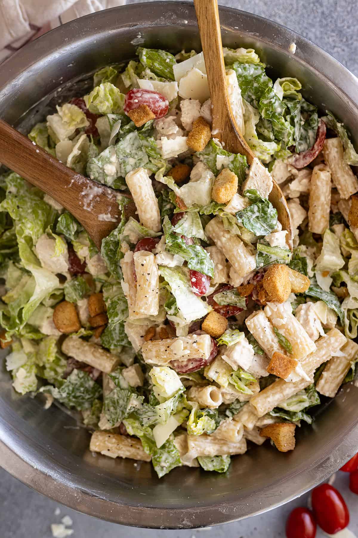 Overhead view of chicken caesar pasta salad in a bowl with spoons ready to serve it.
