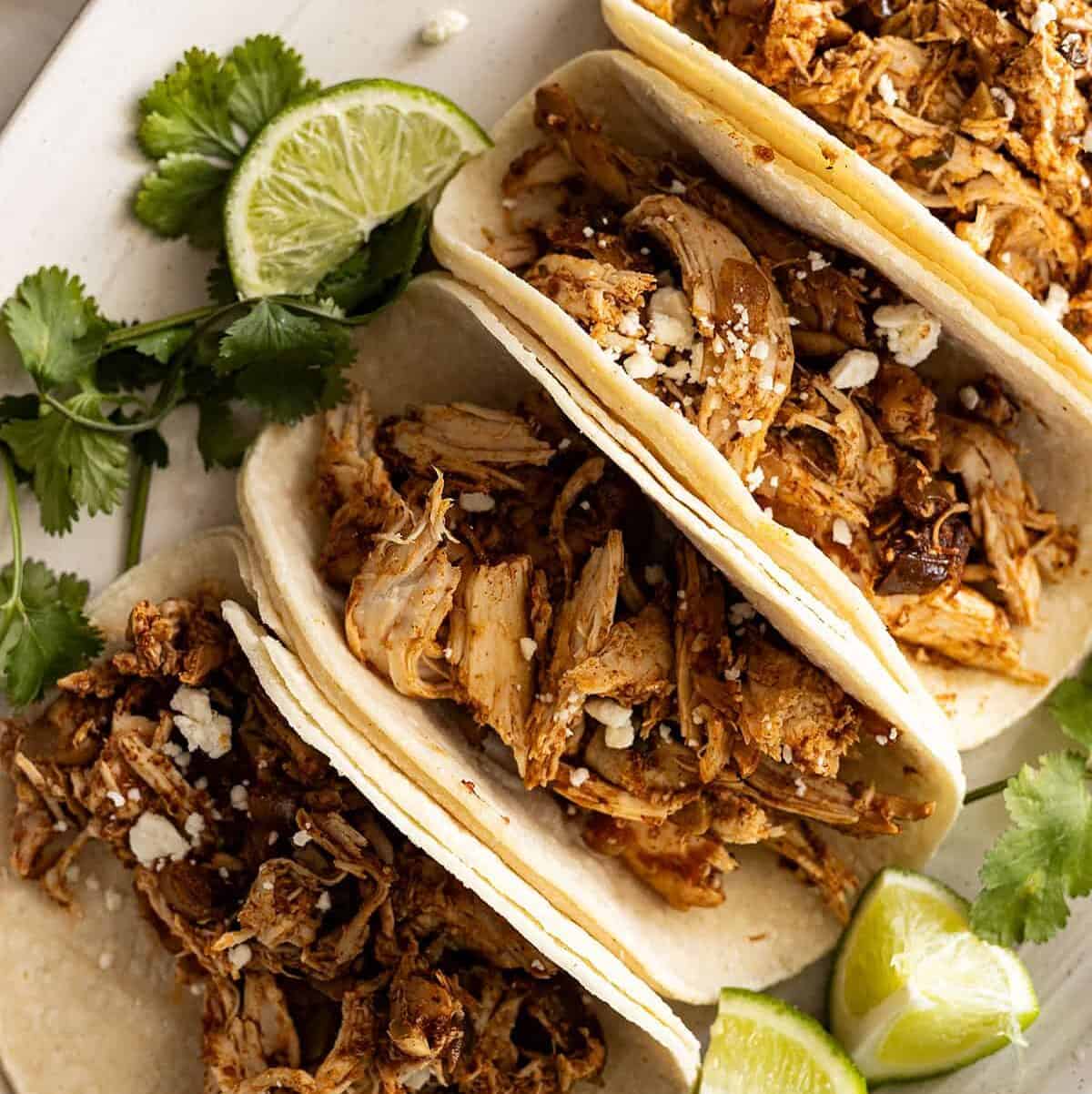Overhead view of tacos on a white plate garnished with white cheese.
