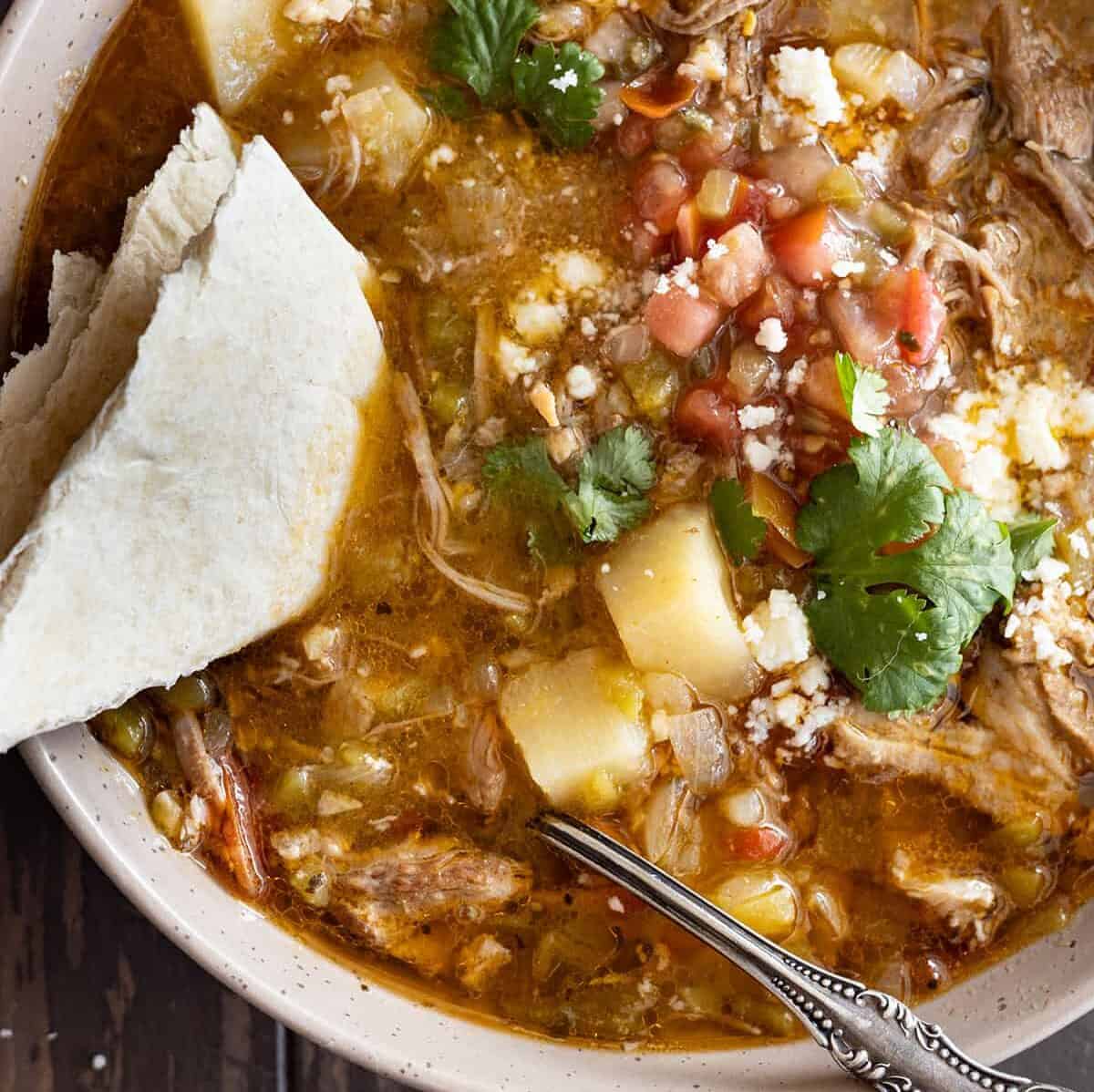 Overhead view of stew in a bowl with a spoon and a tortilla in the soup.