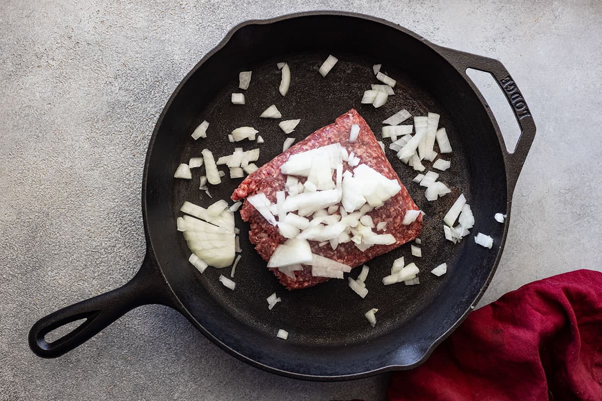 Picture of ground beef and onion in a cast iron skillet.