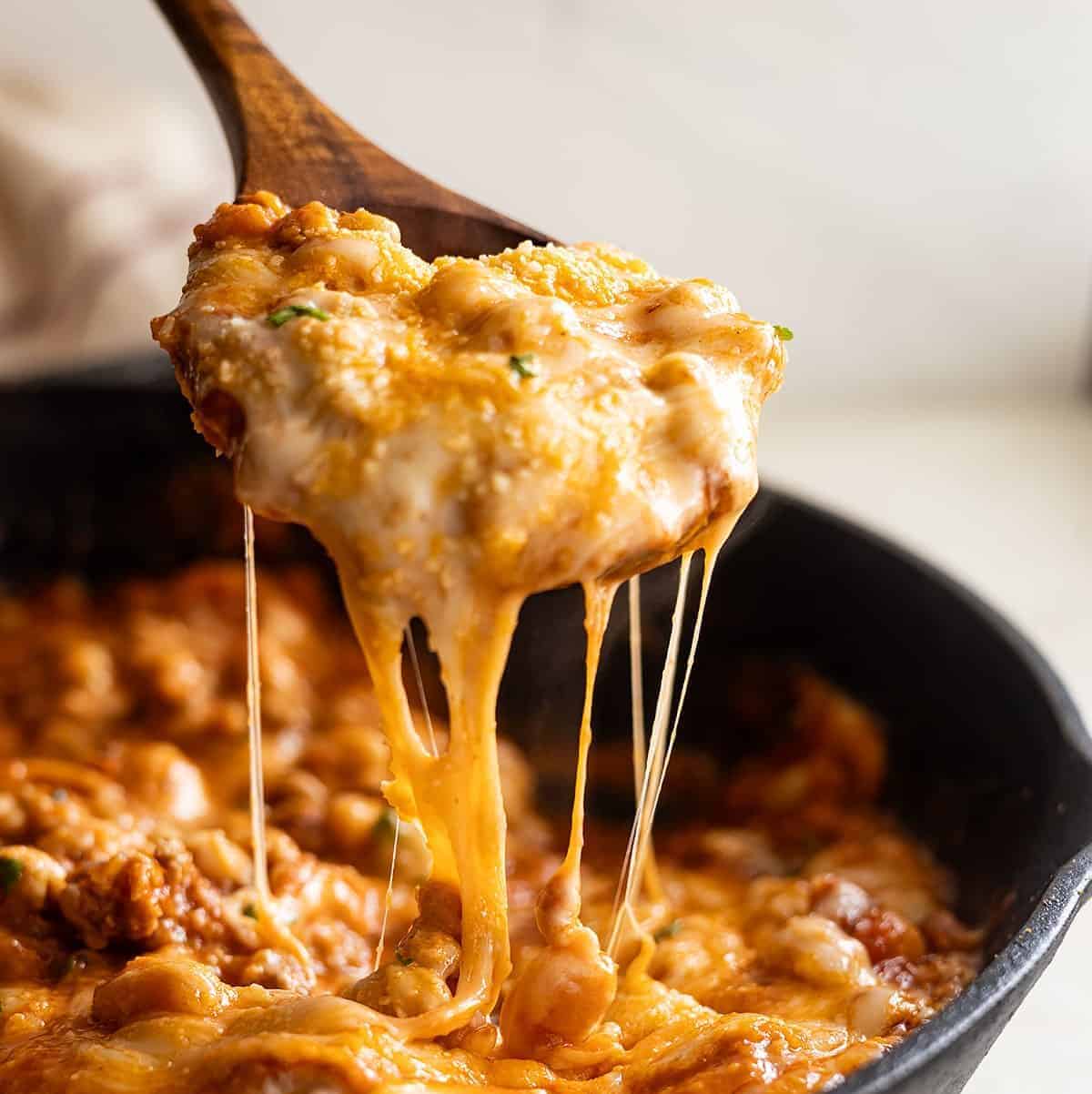 A wooden spoon pulling up a spoonful of beans and has a nice cheese pull.