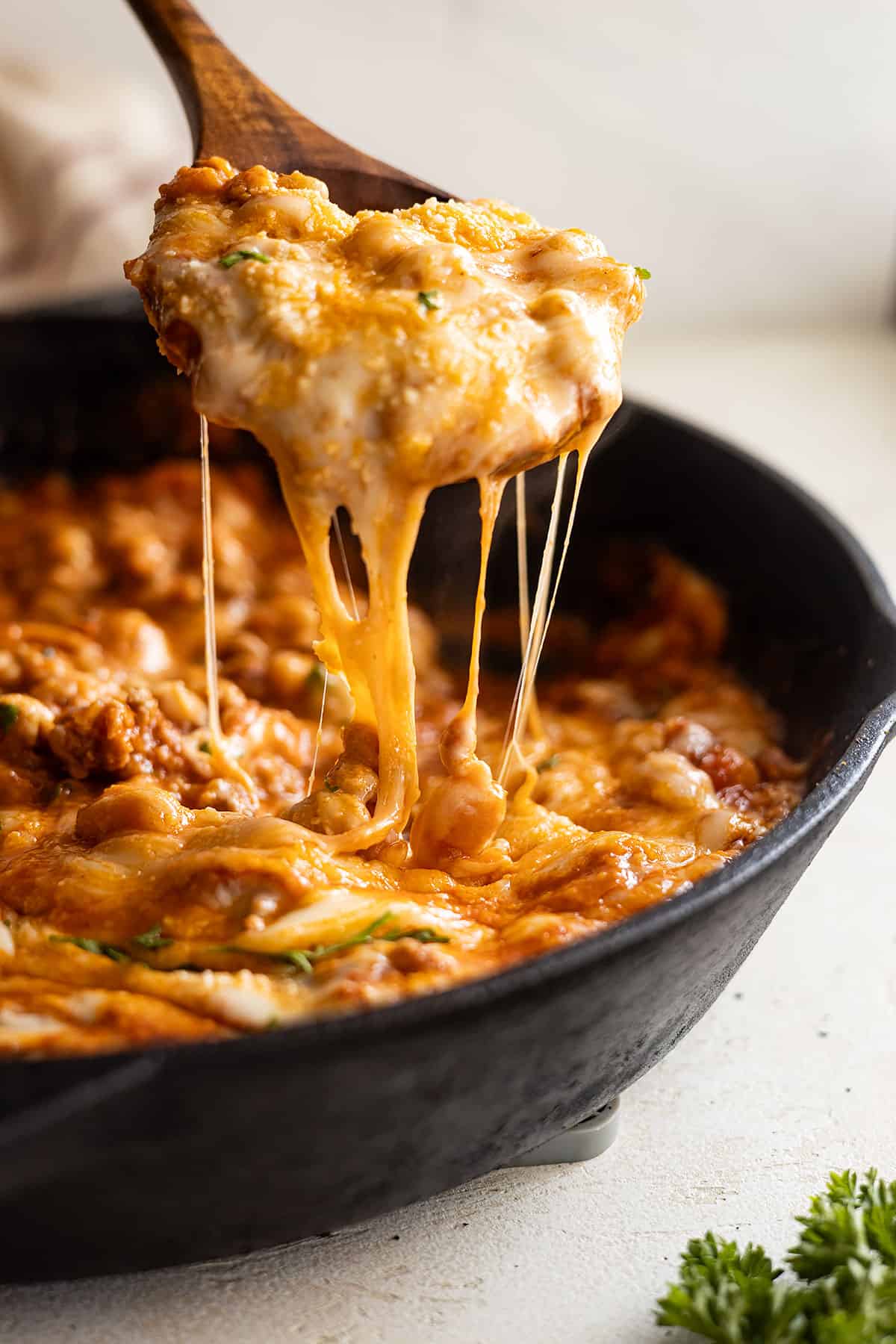 A wooden spoon pulling up a spoonful of beans and has a nice cheese pull.