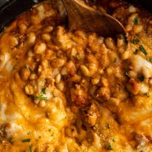 Overhead picture of pizza beans in a skillet with a wooden spoon taking a spoonful out.