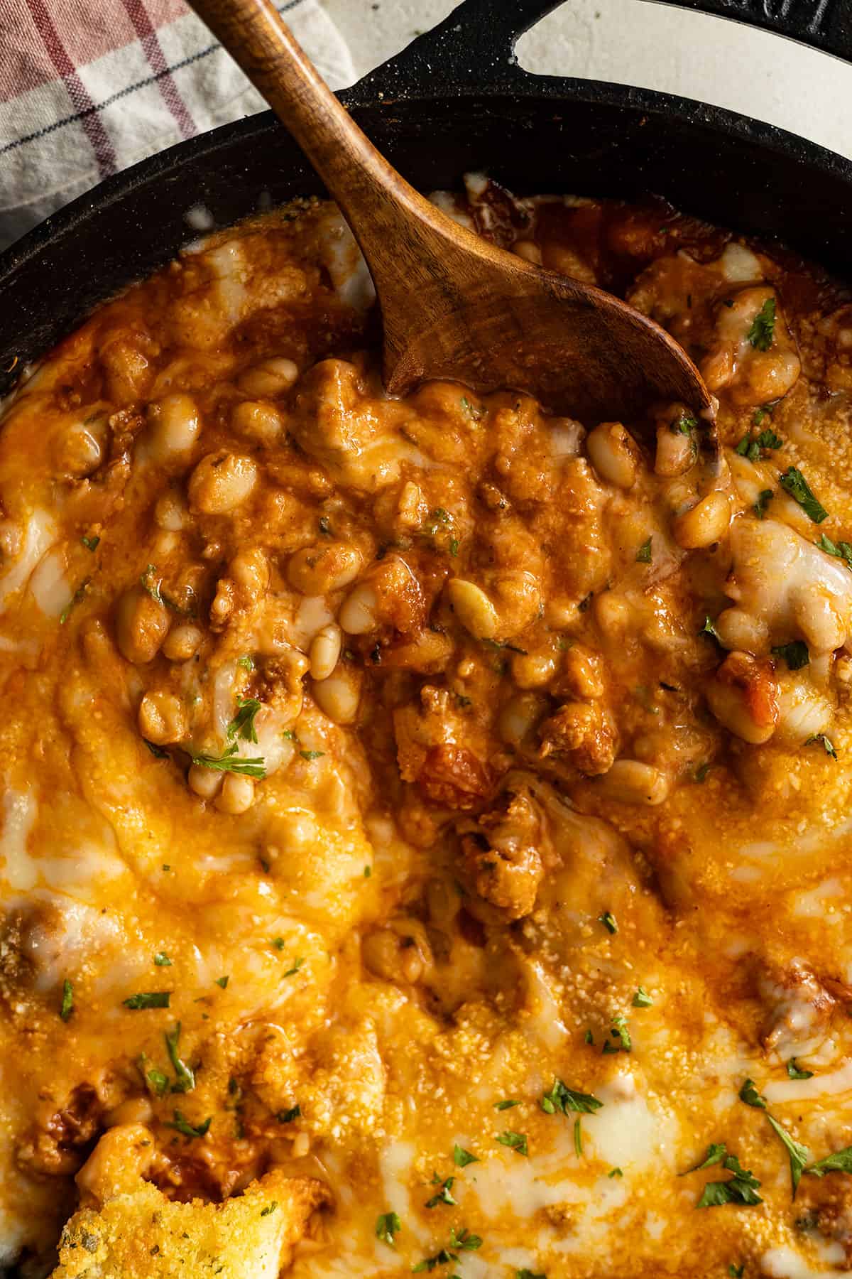 Overhead picture of pizza beans in a skillet with a wooden spoon taking a spoonful out.
